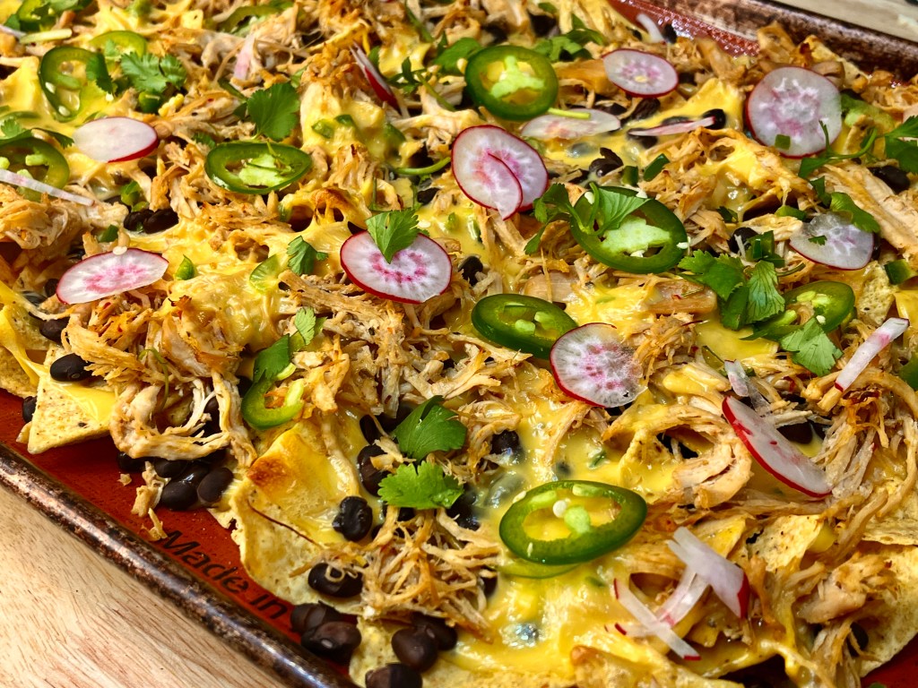 Close up of stacked with homemade queso, black beans, sliced jalapenos, radishes, and onions. garnished with cilantro 