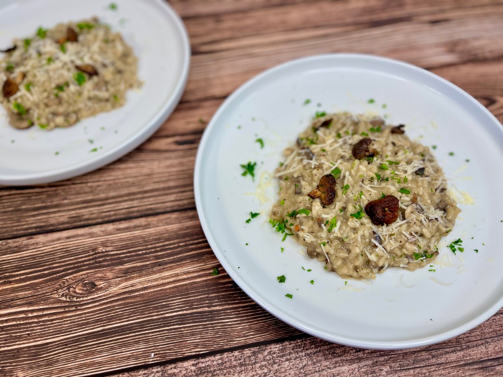 two plates of creamy mushroom risotto. Garnished with parsley, shredded Parmesan and mushrooms  