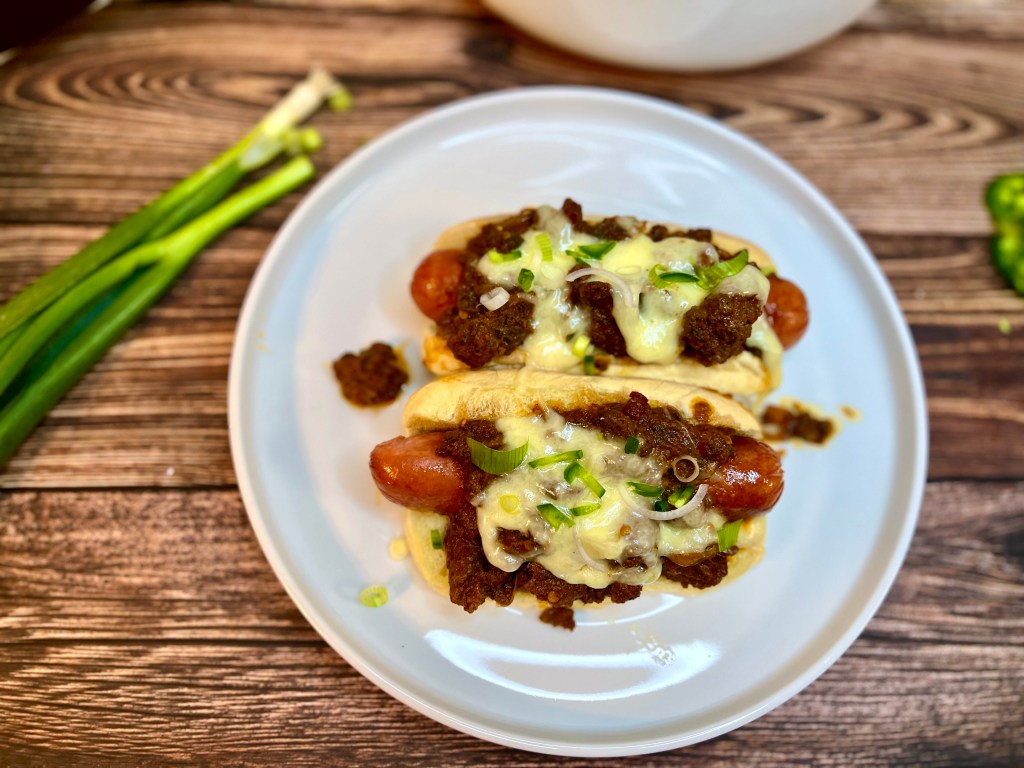 Two chili cheese hot dogs, slathered in chili with melted cheese and onions on top