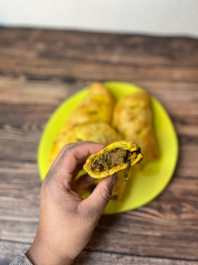 showing a cross section of the hand pie stuffed with ground beef, collard greens and sweet potatoes. All nestled in a flaky and delicately spiced crust.