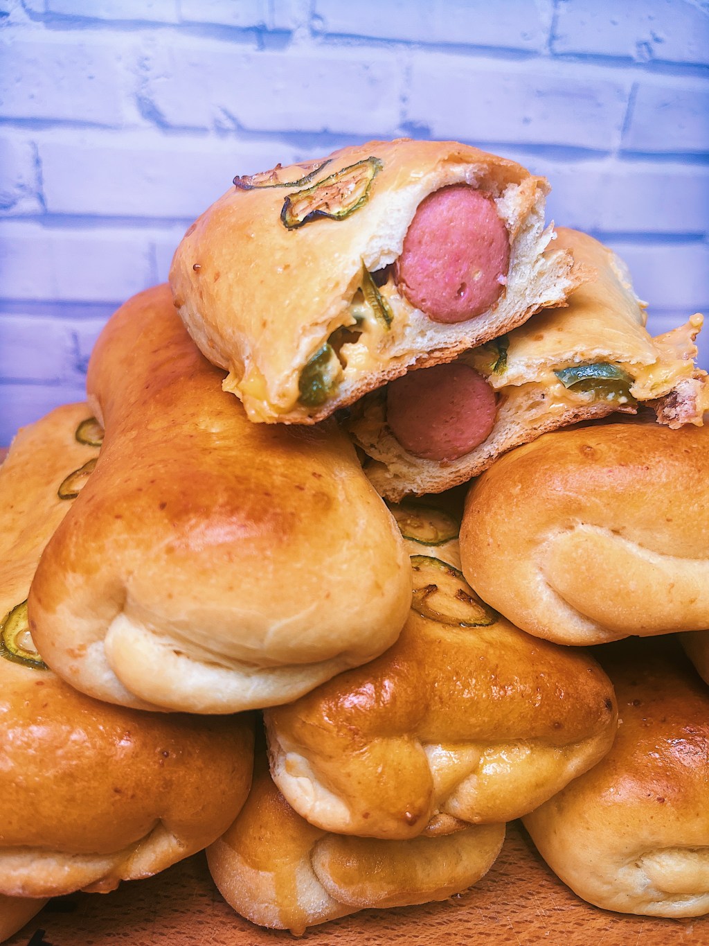 Snack of Kolaches. Golden brown and fluffy with the kolache on the top, cut open. The bisection reveals the filling; a plump sausage with American cheese and jalapeno.